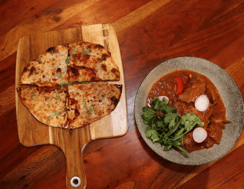 A spicy vindaloo curry served with fluffy naan bread on a plate.