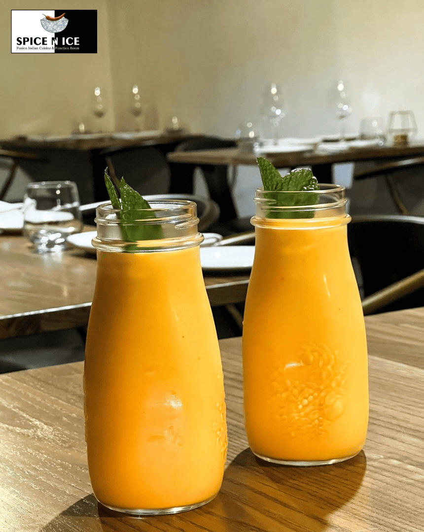 A creamy, smooth mango lassi in a tall glass garnished with mint and a slice of mango.