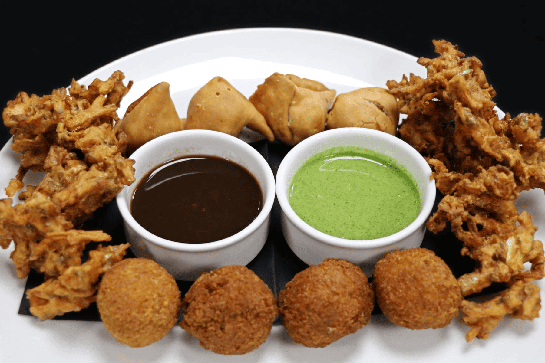 A variety of Indian entrees including fritters, onion bhaji, and samosas, served on a plate.